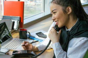 Asian woman working at desk, multitasking with a smile.