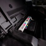 Detailed view of open printer with visible CMYK ink cartridges in a dark setting.